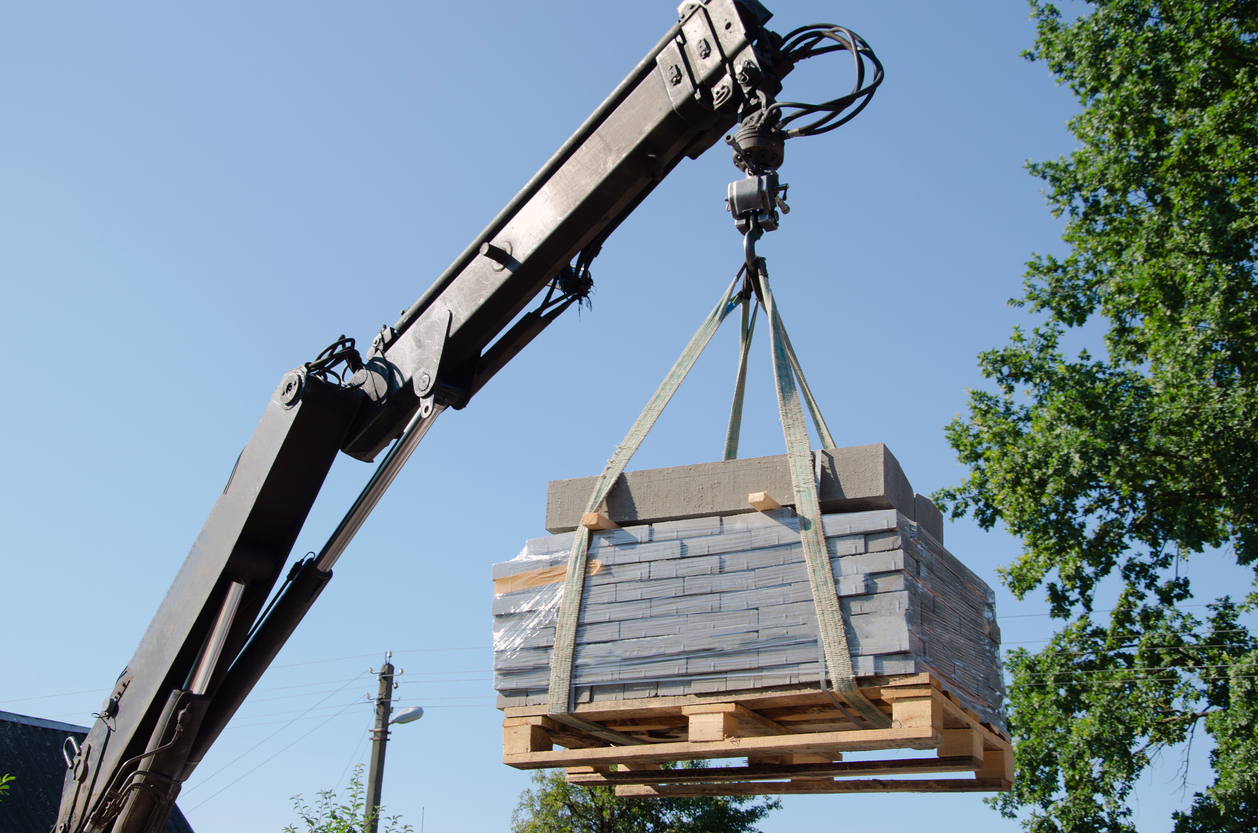 Unloading paving slabs from a truck. Men unload paving slabs using a manipulator. Workers unload building materials from a large machine.